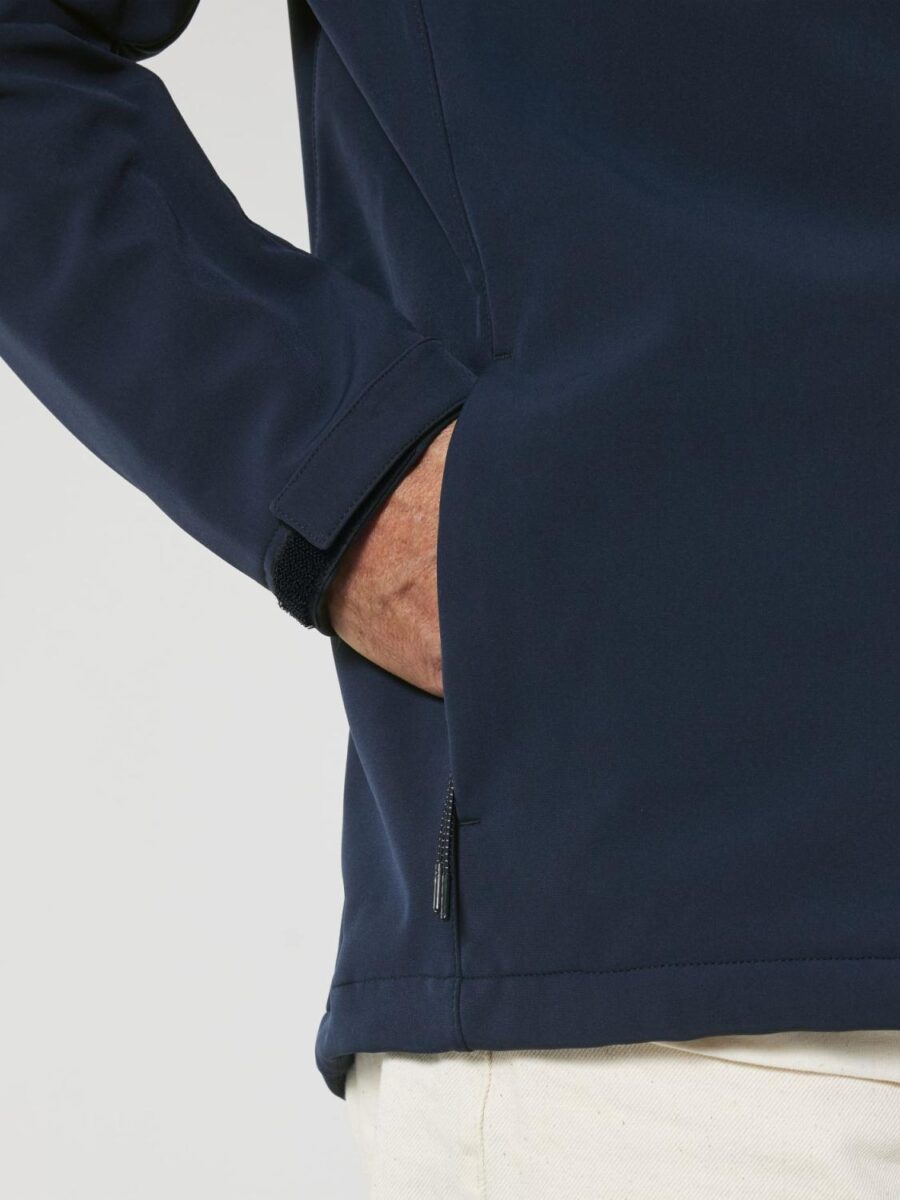 Dettaglio di una giacca blu navy con polsino regolabile dotato di chiusura in velcro per una vestibilità personalizzata. La tasca laterale presenta una zip con cursore doppio rinforzato per garantire sicurezza e praticità durante l’utilizzo.